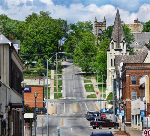 A scenic view of a tree-lined street with buildings, a church, and a clear blue sky in the background.