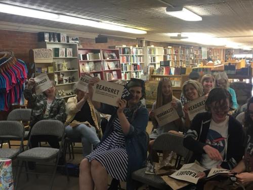 A group of people in a bookstore holding signs with playful words, smiling and engaged in an event.