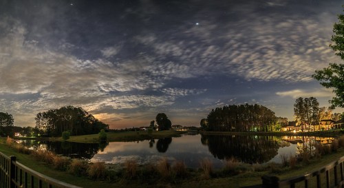 A serene night scene of a lake surrounded by trees, reflecting clouds and stars in the sky.