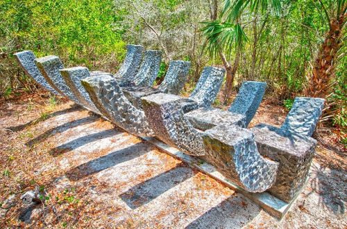 A unique stone sculpture resembling abstract waves, surrounded by lush greenery in a natural setting.