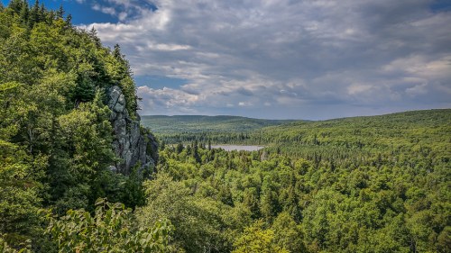 A panoramic view of lush green forests and a serene lake under a partly cloudy sky.