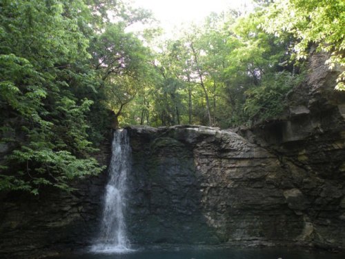 A serene waterfall cascading over rocky cliffs, surrounded by lush green trees and a tranquil pool below.