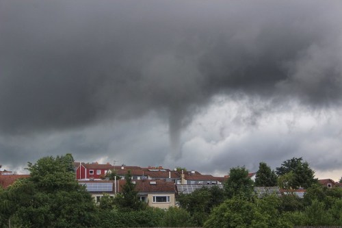 A dark, stormy sky looms over rooftops, with a visible funnel cloud forming in the distance.