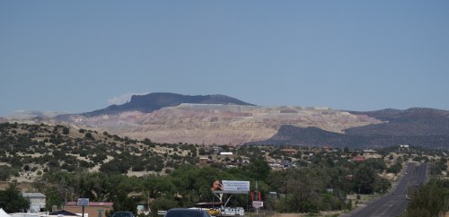 A scenic view of layered mountains with a clear blue sky, featuring a highway and greenery in the foreground.