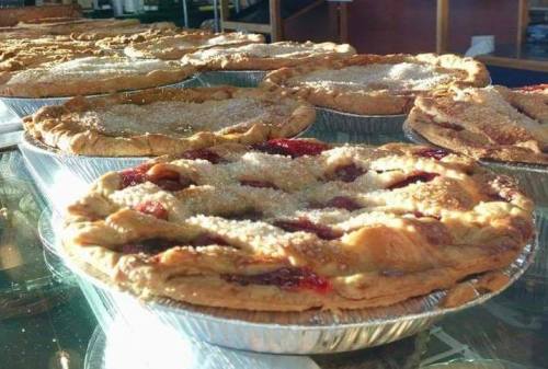 A display of freshly baked fruit pies with golden crusts and a sprinkle of sugar on top, arranged on a glass surface.