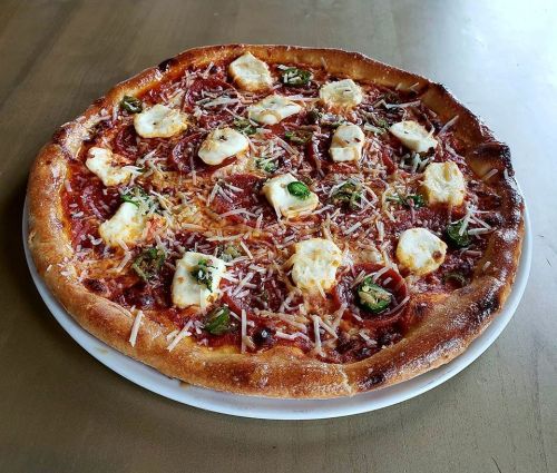 A freshly baked pizza topped with cheese, pepperoni, jalapeños, and herbs on a golden crust, served on a white plate.