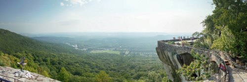 A panoramic view of lush green hills and a cliffside observation area with visitors enjoying the scenery.