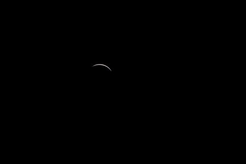 A thin crescent moon against a dark background, creating a serene and minimalist night sky scene.