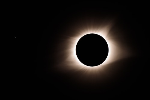 A solar eclipse with a darkened sun surrounded by a glowing halo and faint stars in the background.