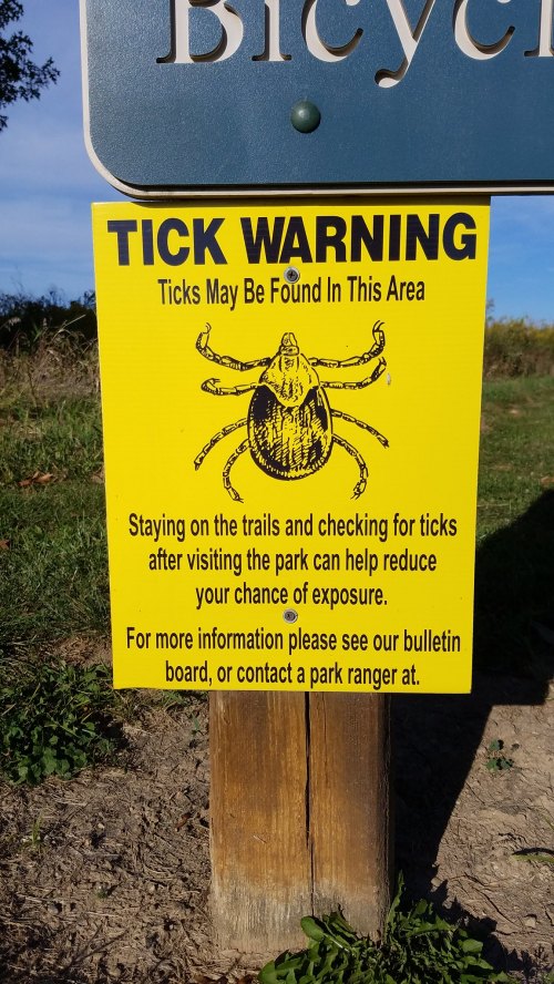 Yellow sign warning about ticks in the area, advising to check for ticks after visiting the park.