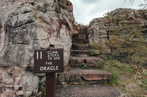 A wooden sign reads "Climb steps to see the Oracle" next to rocky steps leading upward.