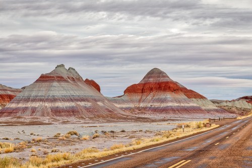 Colorful striped rock formations rise beside a deserted road under a cloudy sky.
