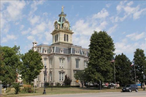Historic courthouse with a clock tower, surrounded by trees and flags, under a partly cloudy sky.