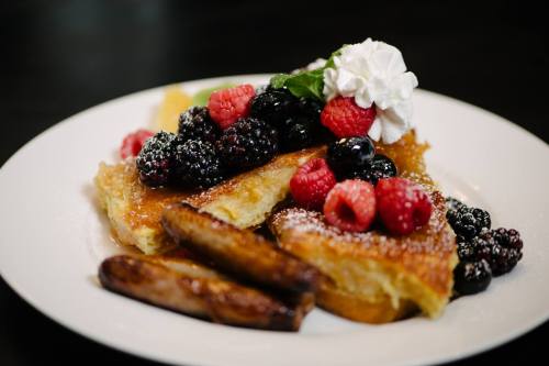 A plate of French toast topped with mixed berries and whipped cream, accompanied by two sausage links.