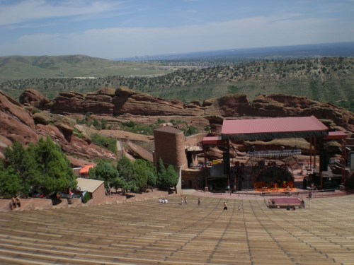 A panoramic view of Red Rocks Amphitheatre, surrounded by rocky hills and greenery under a clear blue sky.