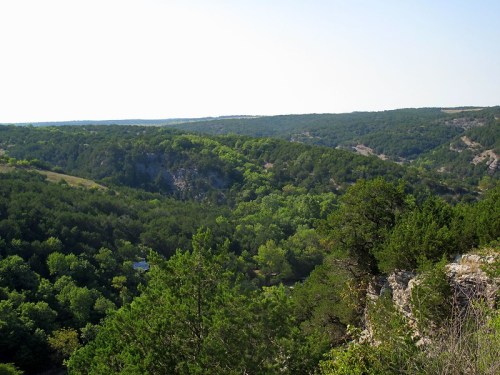 Lush green hills and valleys stretch across the landscape under a clear blue sky.