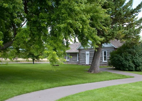 A log cabin surrounded by lush green grass and trees, with a winding path leading to the entrance.