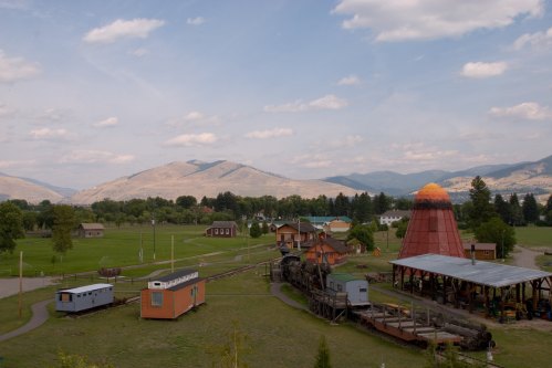 A scenic view of a rural landscape with mountains, colorful buildings, and a vintage train on tracks.