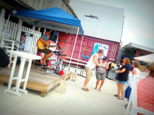 A musician plays guitar under a tent while people dance and socialize at an outdoor venue.