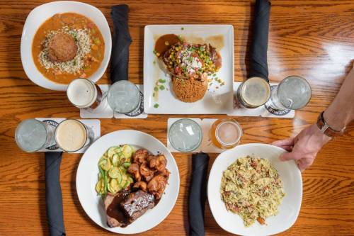 A table set with various dishes: rice, grilled chicken, salad, and drinks, all arranged on a wooden surface.
