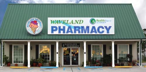A storefront of Waveland Pharmacy featuring a green roof and a colorful ice cream logo.