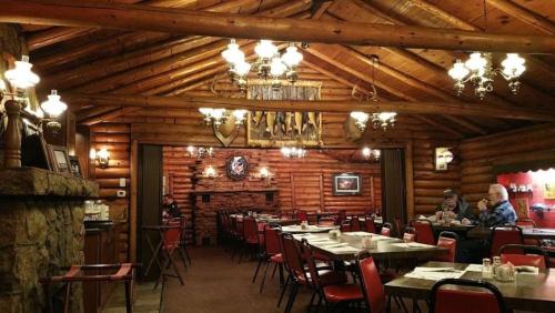 Cozy log cabin restaurant interior with wooden beams, rustic decor, and red chairs around empty tables.