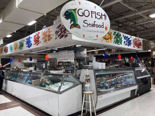 A seafood market stall named "GO FISH" featuring glass display cases filled with fresh seafood and colorful decorations.