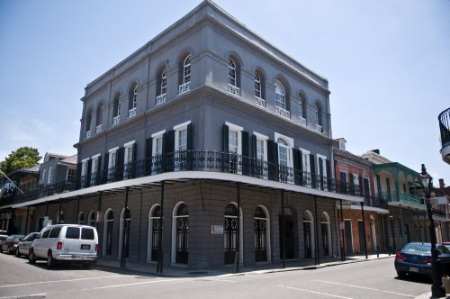 Historic gray building with arched windows and a balcony, located on a sunny street in New Orleans.