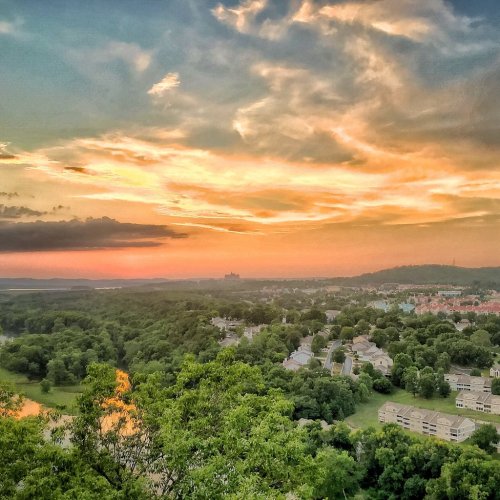 A scenic view of a sunset over a lush landscape, with clouds and a distant city skyline.