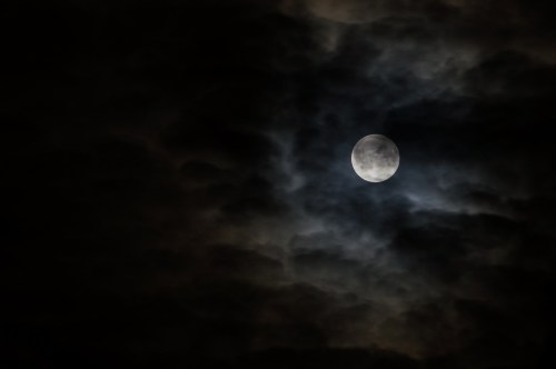 A bright full moon partially obscured by dark, swirling clouds in a night sky.