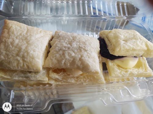 A close-up of flaky pastry squares filled with cream and fruit preserves, arranged in a clear plastic container.