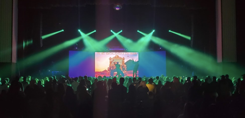 A crowd at a concert with green stage lights and a backdrop featuring "The Golden Child" artwork.