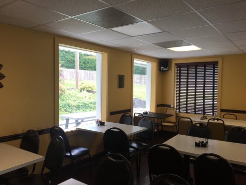 Interior of a casual dining area with empty tables and chairs, featuring large windows and yellow walls.