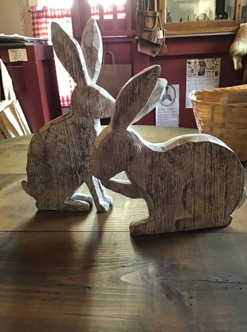 Two wooden rabbit figurines with a rustic finish, positioned on a wooden table in a cozy interior setting.