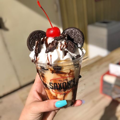 A hand holding a delicious sundae topped with whipped cream, chocolate syrup, Oreos, and a cherry.