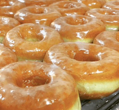Freshly glazed donuts arranged on a cooling rack, showcasing their shiny, golden-brown glaze.