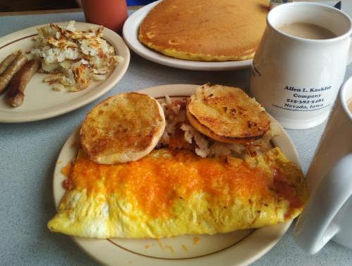 A hearty breakfast plate featuring an omelet with cheese, hash browns, sausage, English muffins, and a coffee mug.
