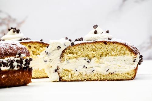 A sliced cake filled with cream and chocolate chips, topped with whipped cream and more chocolate chips.