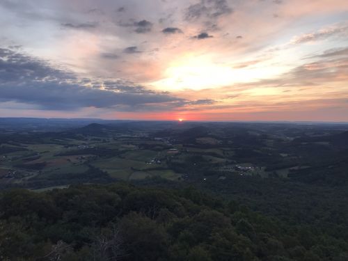 A scenic view of rolling hills and valleys under a colorful sunset sky, with clouds scattered above.