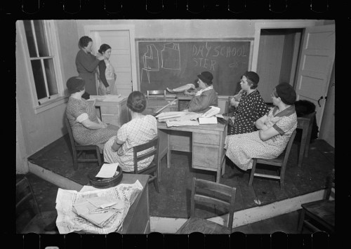 A vintage classroom scene with women seated at desks, one teaching at a chalkboard, surrounded by papers and books.