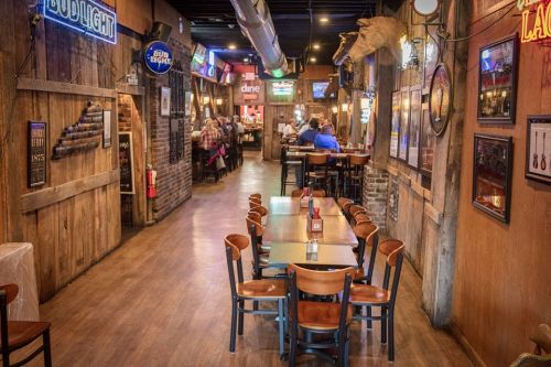 A rustic restaurant interior with wooden walls, tables, and neon signs, bustling with diners in the background.