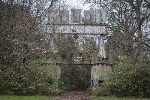 A weathered, abandoned entrance sign surrounded by overgrown trees and foliage.