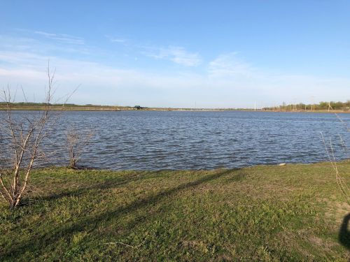 A calm river scene with gentle waves, grassy banks, and a clear blue sky in the background.