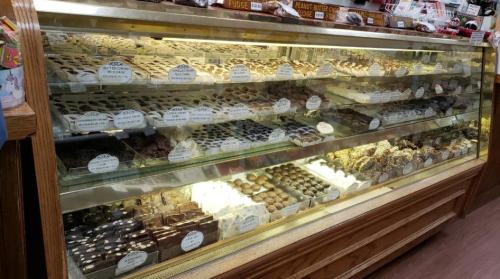 A display case filled with various chocolates and confections, labeled with names and prices.