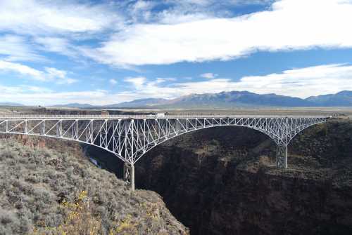 A large white bridge spans a deep canyon, with mountains and a blue sky in the background.