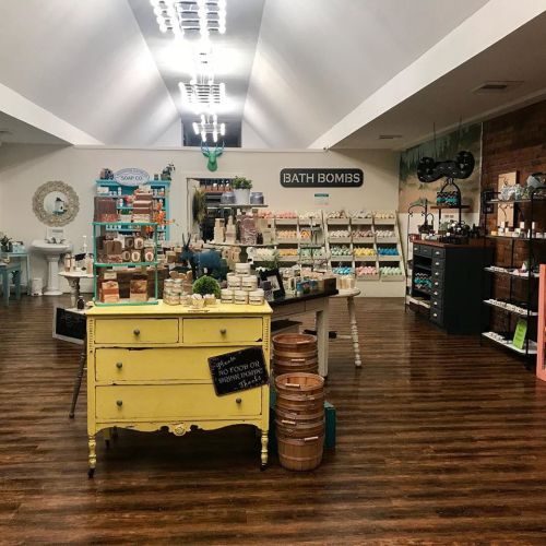 A bright, inviting shop interior featuring shelves of bath products, a yellow dresser, and wooden accents.