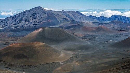 A panoramic view of volcanic craters and rugged mountains under a clear blue sky with distant clouds.