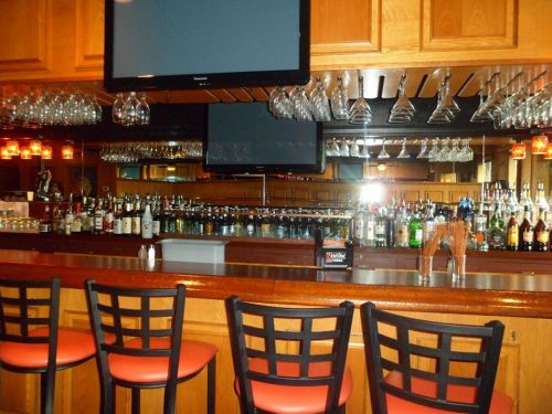 A well-stocked bar with a wooden counter, hanging glasses, and multiple bottles displayed on shelves.