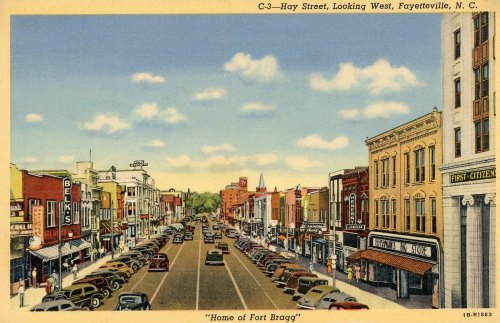 Vintage postcard of Hay Street in Fayetteville, NC, showcasing shops, cars, and a clear blue sky. "Home of Fort Bragg."
