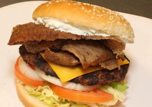 A hearty burger with a sesame seed bun, layered with cheese, lettuce, tomato, onions, and sliced meat.